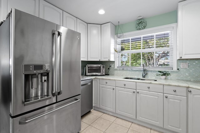 kitchen with sink, light tile patterned floors, stainless steel appliances, decorative backsplash, and white cabinets