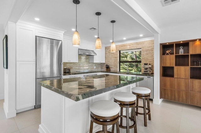 kitchen featuring hanging light fixtures, appliances with stainless steel finishes, white cabinetry, a kitchen island, and under cabinet range hood