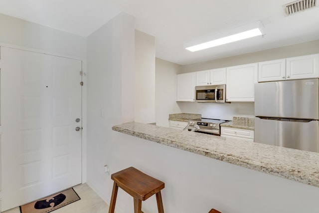 kitchen with a breakfast bar area, appliances with stainless steel finishes, white cabinetry, light stone countertops, and kitchen peninsula