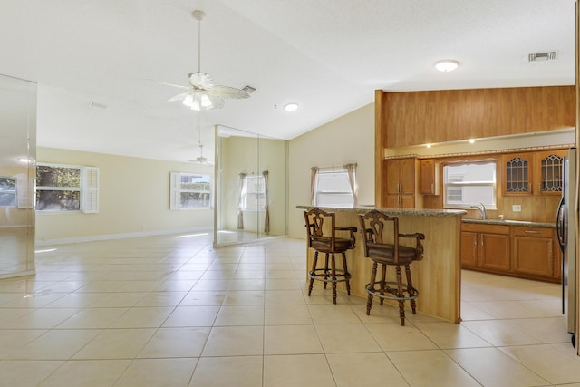 kitchen featuring stone counters, lofted ceiling, a breakfast bar area, light tile patterned floors, and ceiling fan