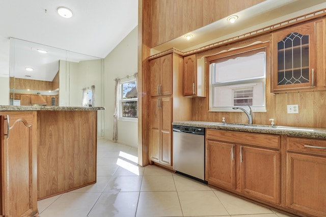 kitchen with lofted ceiling, sink, stainless steel dishwasher, light tile patterned floors, and light stone counters