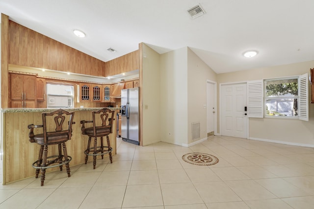 kitchen with stainless steel fridge with ice dispenser, lofted ceiling, a breakfast bar area, light tile patterned floors, and kitchen peninsula