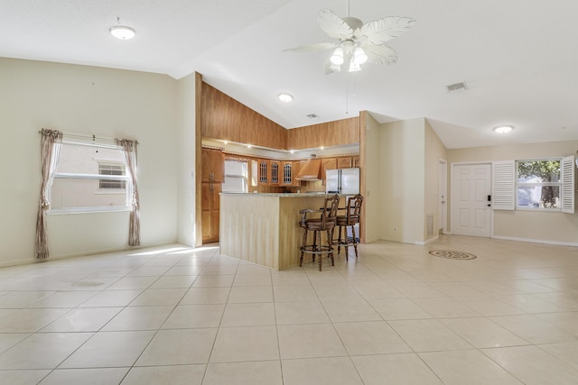 kitchen with vaulted ceiling, a breakfast bar area, fridge, light tile patterned floors, and kitchen peninsula