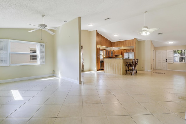 unfurnished living room featuring light tile patterned floors, a textured ceiling, high vaulted ceiling, and ceiling fan