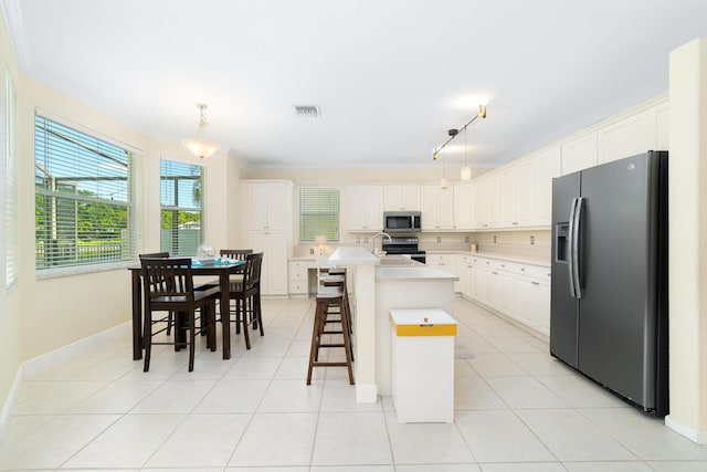 kitchen featuring pendant lighting, light tile patterned floors, appliances with stainless steel finishes, a kitchen breakfast bar, and an island with sink