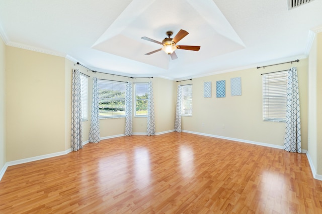 empty room with crown molding, a raised ceiling, ceiling fan, and light wood-type flooring