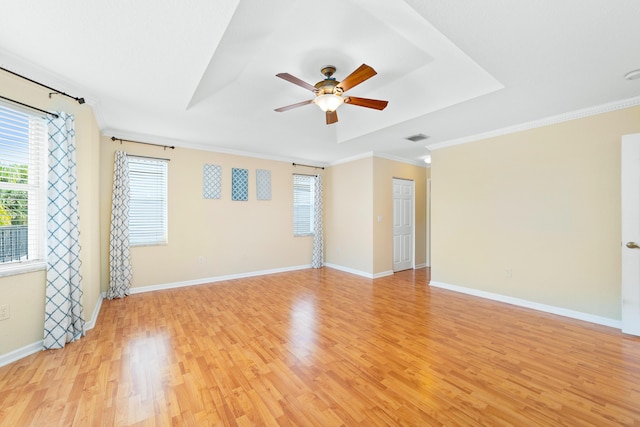 empty room with ceiling fan, ornamental molding, a tray ceiling, and light hardwood / wood-style floors