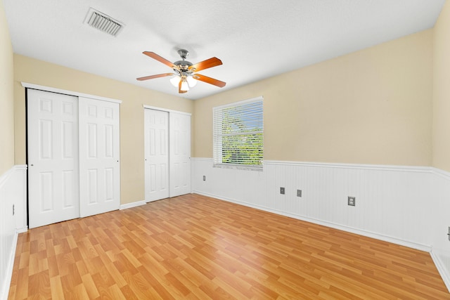 unfurnished bedroom featuring ceiling fan, light wood-type flooring, and two closets