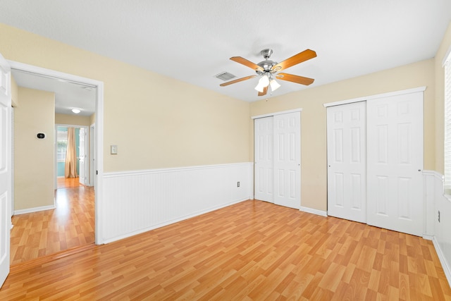 unfurnished bedroom with two closets, ceiling fan, and light wood-type flooring