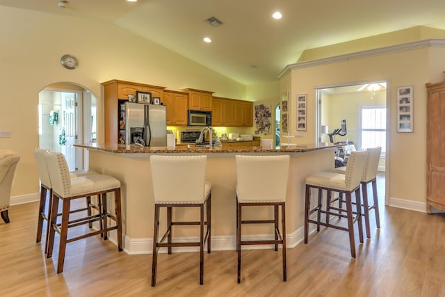 kitchen with a kitchen bar, vaulted ceiling, light hardwood / wood-style floors, and appliances with stainless steel finishes