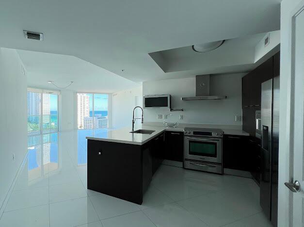 kitchen featuring sink, light tile patterned floors, wall chimney exhaust hood, kitchen peninsula, and stainless steel electric range