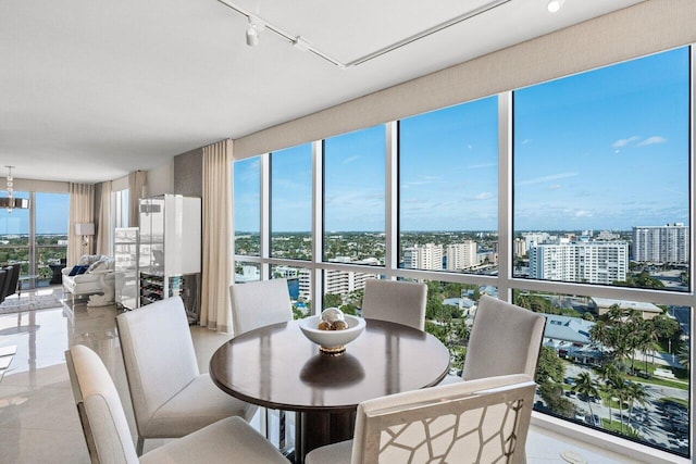 dining space featuring rail lighting, a notable chandelier, a wall of windows, and a city view