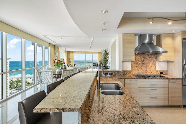 kitchen featuring black stovetop, a water view, a sink, wall chimney range hood, and a kitchen bar