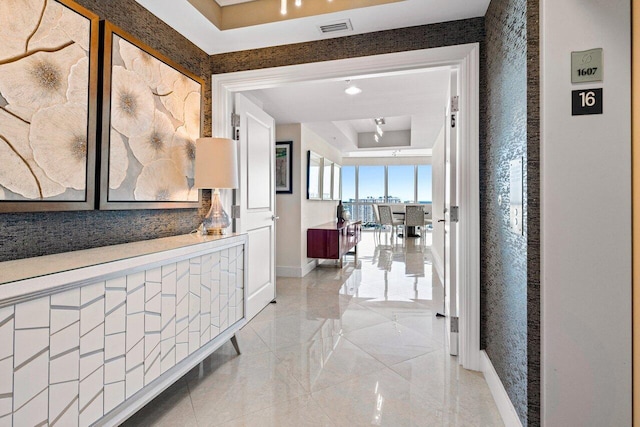 corridor with visible vents, a tray ceiling, and baseboards