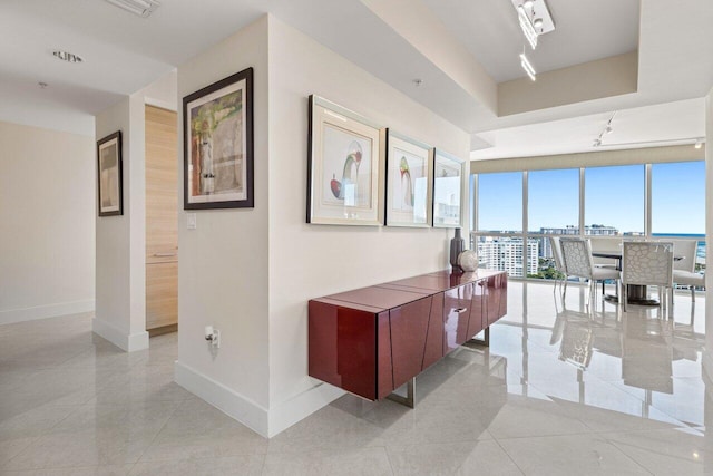 hall with light tile patterned floors, baseboards, a wall of windows, and a tray ceiling