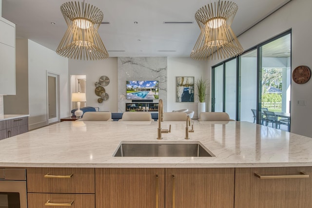 kitchen featuring sink, light stone countertops, an island with sink, and oven