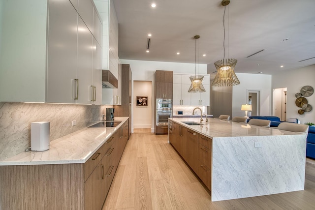 kitchen with sink, white cabinetry, a large island with sink, pendant lighting, and black electric stovetop