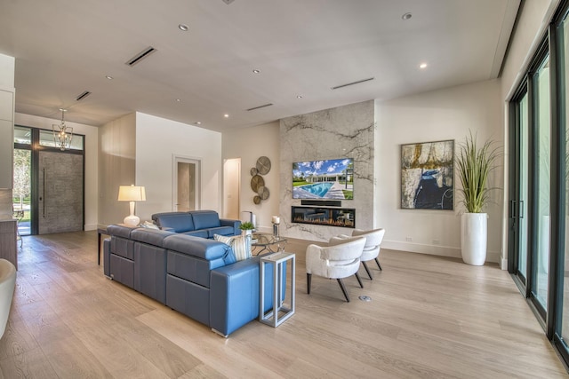 living room with a large fireplace, an inviting chandelier, and light hardwood / wood-style flooring