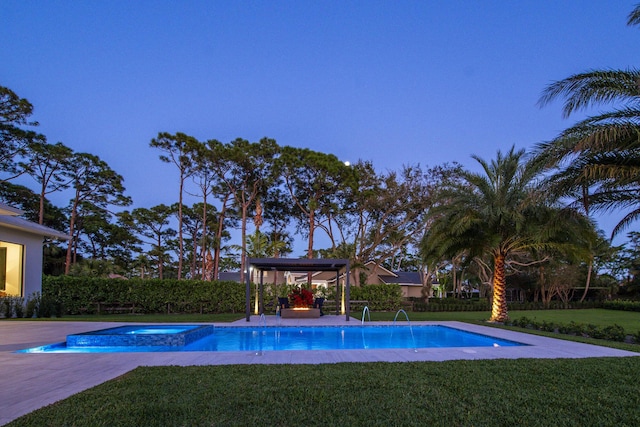 pool at dusk featuring an in ground hot tub and a lawn