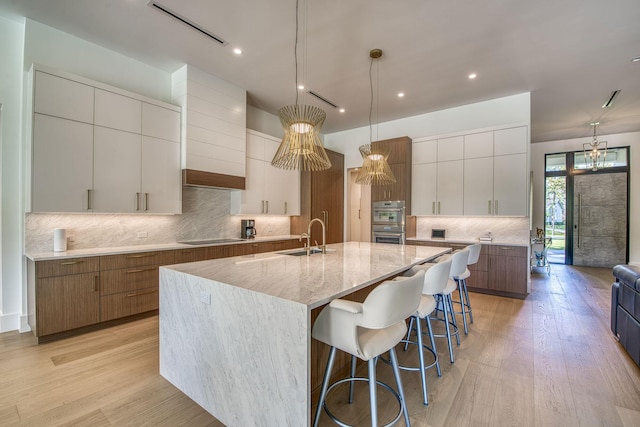 kitchen featuring pendant lighting, sink, white cabinetry, black electric cooktop, and a large island with sink