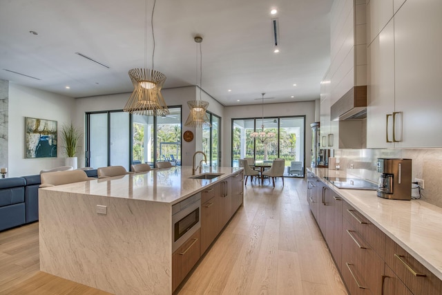 kitchen with light stone counters, decorative light fixtures, sink, and a large island with sink