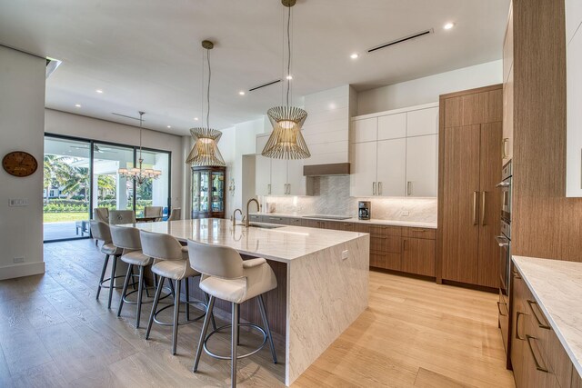 kitchen with sink, a spacious island, light stone countertops, white cabinets, and decorative light fixtures