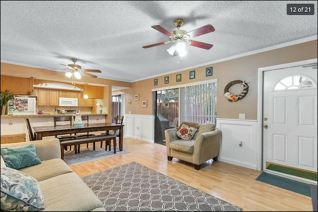 living room featuring ceiling fan, ornamental molding, a textured ceiling, and light wood-type flooring