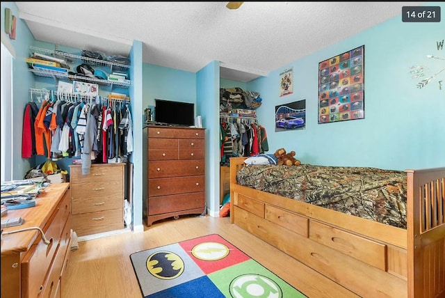 bedroom with a walk in closet, a closet, a textured ceiling, and light wood-type flooring