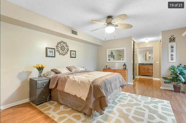 bedroom with ceiling fan, a textured ceiling, light hardwood / wood-style floors, and ensuite bath