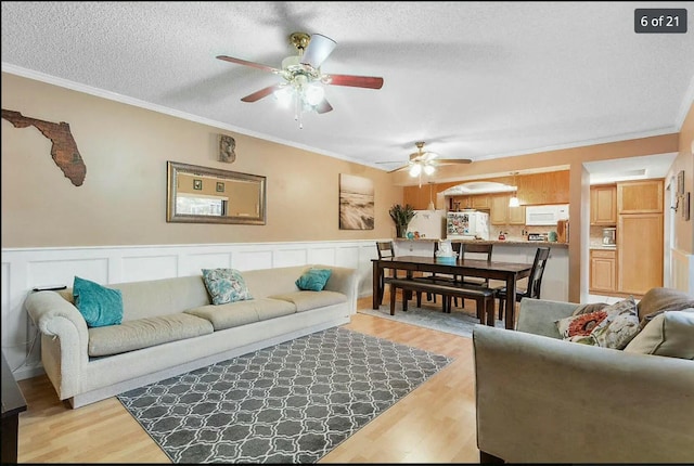 living room with ceiling fan, ornamental molding, light hardwood / wood-style floors, and a textured ceiling