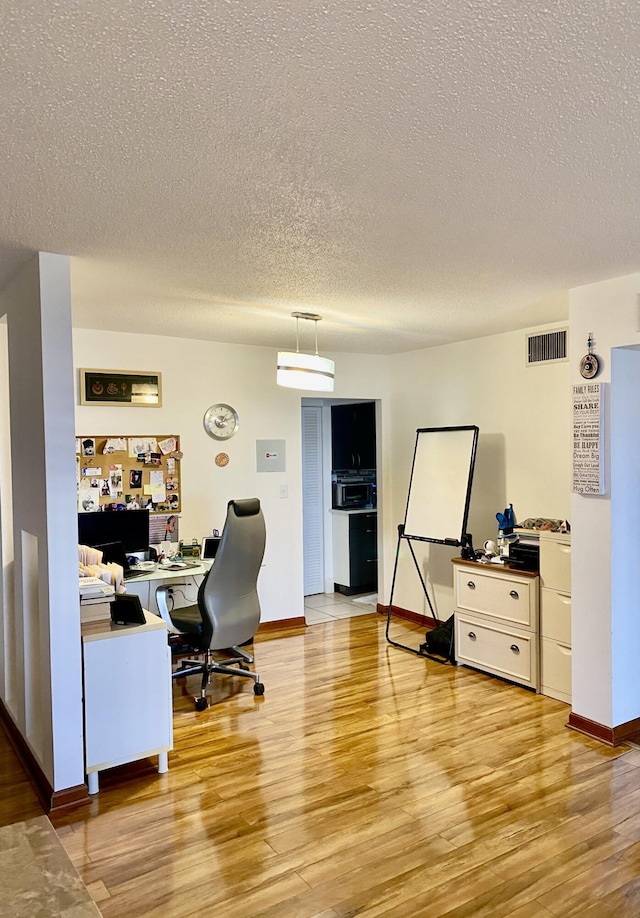 home office with a textured ceiling and light hardwood / wood-style flooring