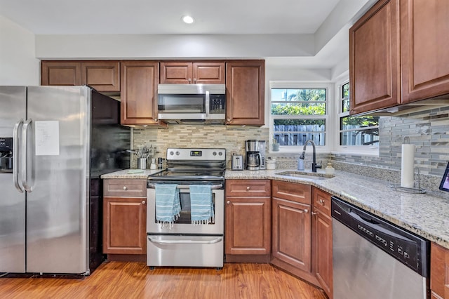 kitchen with appliances with stainless steel finishes, tasteful backsplash, sink, light stone countertops, and light wood-type flooring