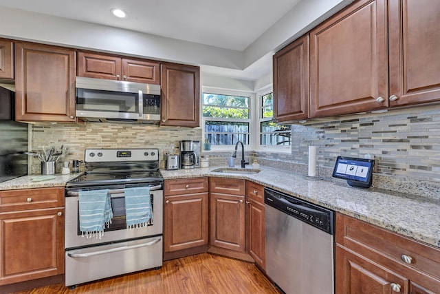 kitchen featuring sink, appliances with stainless steel finishes, light stone counters, tasteful backsplash, and light wood-type flooring