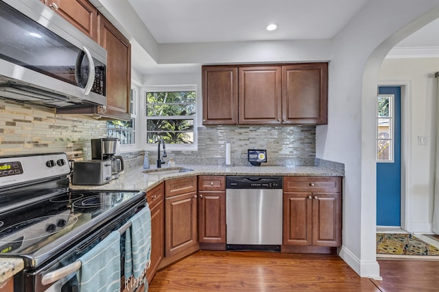 kitchen featuring sink, hardwood / wood-style flooring, appliances with stainless steel finishes, light stone counters, and decorative backsplash