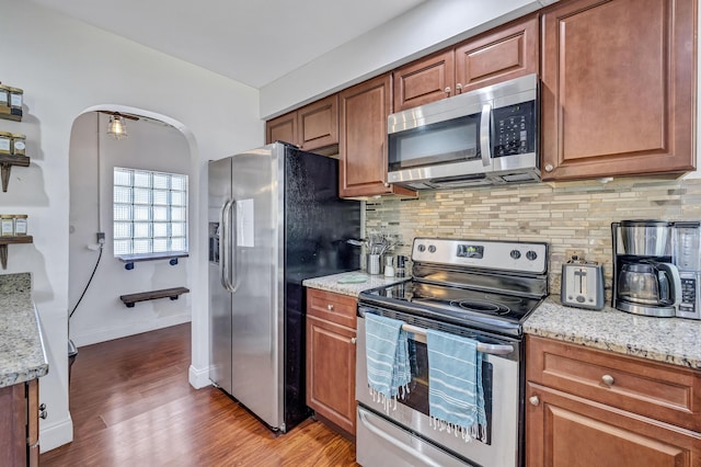 kitchen featuring light stone countertops, backsplash, stainless steel appliances, and light wood-type flooring