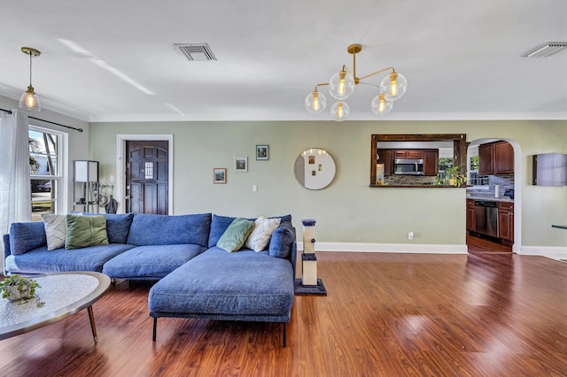 living room featuring dark wood-type flooring, ornamental molding, and a notable chandelier