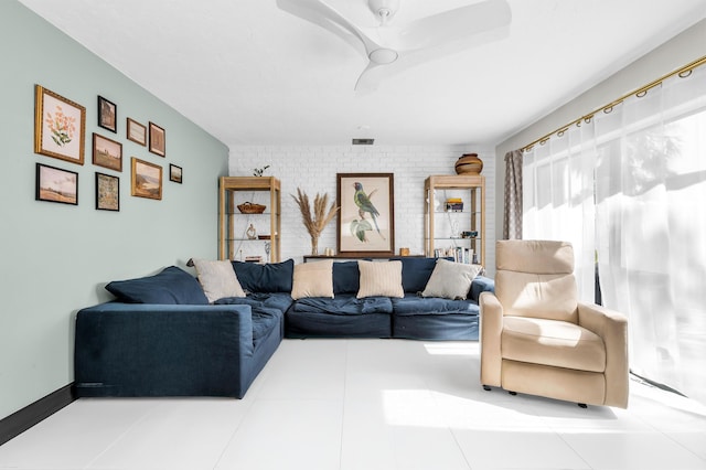 living room with tile patterned floors, ceiling fan, and brick wall