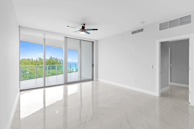 spare room featuring visible vents, marble finish floor, a ceiling fan, a wall of windows, and baseboards