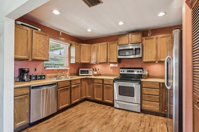 kitchen featuring sink, light hardwood / wood-style flooring, stainless steel appliances, and a textured ceiling