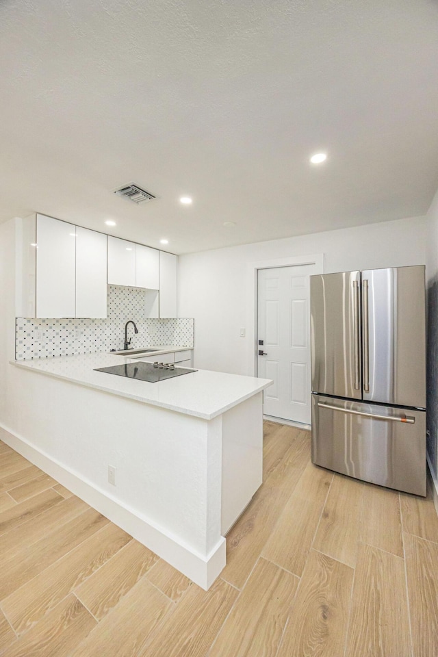 kitchen featuring white cabinetry, stainless steel fridge, decorative backsplash, kitchen peninsula, and light wood-type flooring