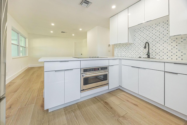 kitchen with tasteful backsplash, light hardwood / wood-style floors, white cabinets, kitchen peninsula, and stainless steel oven