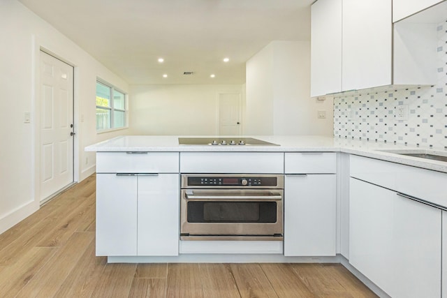 kitchen with white cabinetry, kitchen peninsula, stainless steel oven, and light wood-type flooring