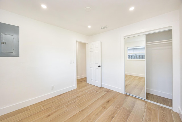 unfurnished bedroom with electric panel, light wood-type flooring, and a closet