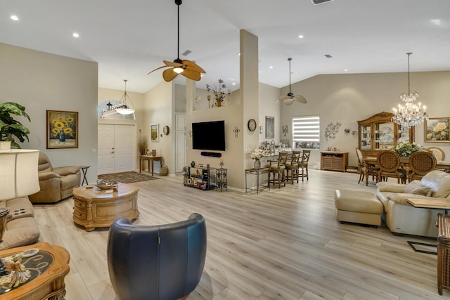 living room with high vaulted ceiling, ceiling fan with notable chandelier, and light hardwood / wood-style floors