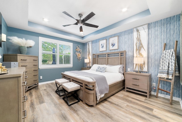 bedroom featuring wallpapered walls, baseboards, a raised ceiling, and light wood finished floors