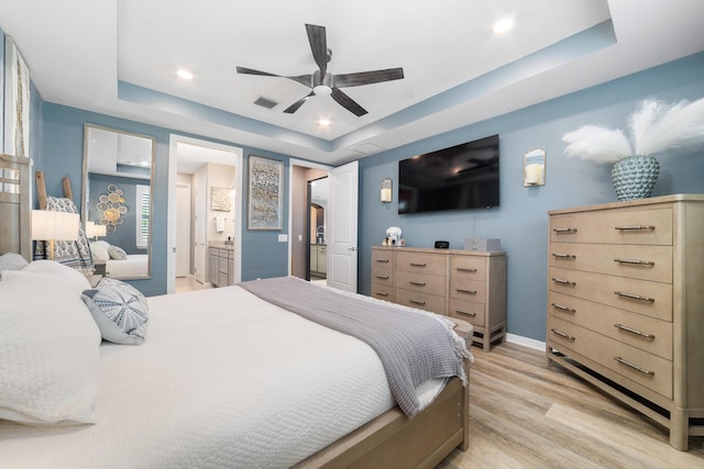 bedroom with light wood finished floors, visible vents, ensuite bath, and a tray ceiling