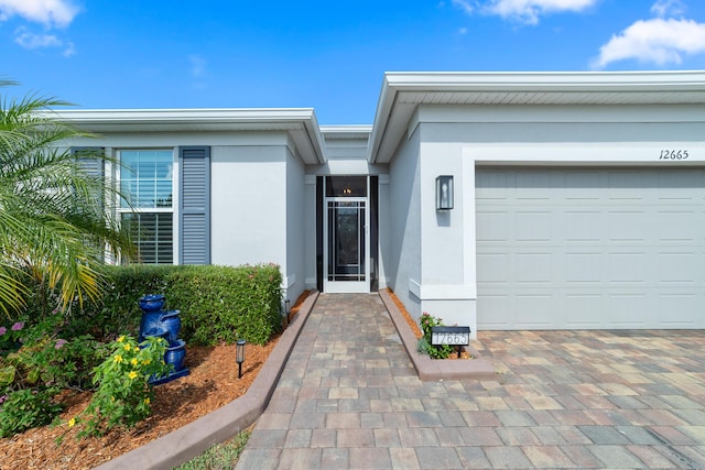 doorway to property with stucco siding, an attached garage, and driveway