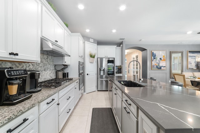kitchen featuring under cabinet range hood, a sink, stainless steel appliances, arched walkways, and light tile patterned flooring