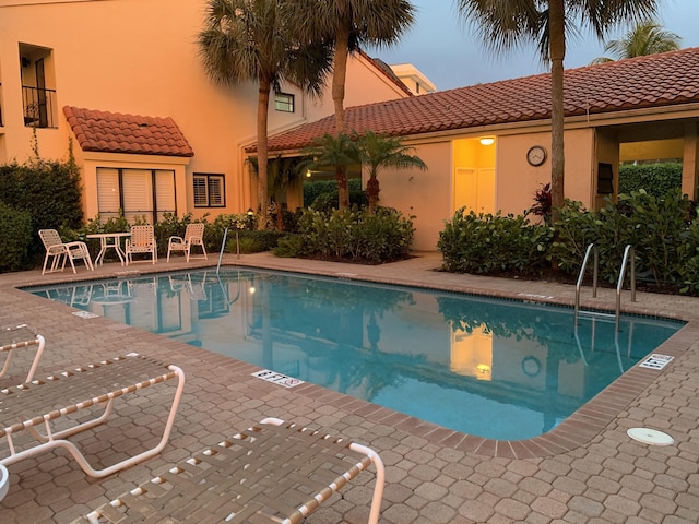 pool at dusk featuring a patio area and a community pool