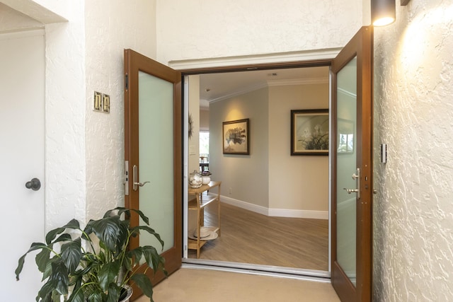 hall featuring baseboards, a textured wall, wood finished floors, and crown molding